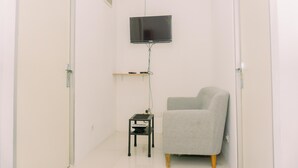 A small, sparsely furnished room with a television mounted on the wall, a small table with a chair, and a door on one side. - Comfort 2Br At 22Nd Floor Menara Kebon Jeruk Apartment (Jakarta)