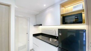 A compact kitchen with white cabinets, a black refrigerator, a stainless steel sink, and a microwave on a wooden shelf. - Nice And Comfortable 2Br At 20Th Floor Tokyo Riverside Apartment (Teluknaga)