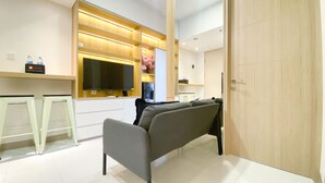 A modern hotel room with a sofa, a flat-screen TV, a water dispenser, and a wooden wardrobe. - Nice And Comfortable 2Br At 20Th Floor Tokyo Riverside Apartment (Teluknaga)