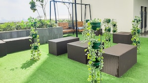 A rooftop terrace with artificial grass, wicker furniture, and potted plants. - Best Homey Studio Apartment At B Residence (Pagedangan)
