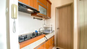 Una cucina compatta con mobili in legno, un fornello a gas, un forno integrato, un telefono fissato al muro e un lavandino con un portabiancheria.