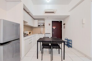 Cocina compacta con refrigerador, microondas y lavamanos. Hay una mesa de comedor con sillas y un pequeño estante azul.