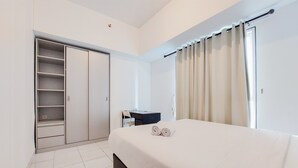 A hotel room with a bed, a desk, a chair, a wardrobe, and a window with curtains. - Best Modern 2Br At Casa De Parco Apartment (South Tangerang)
