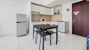 A compact kitchen with white cabinets, a black dining table with four chairs, a refrigerator, a microwave, and a water dispenser. - Best Modern 2Br At Casa De Parco Apartment (South Tangerang)