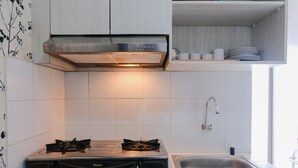 A kitchen with a gas stove, a stainless steel sink, and white tiled walls.