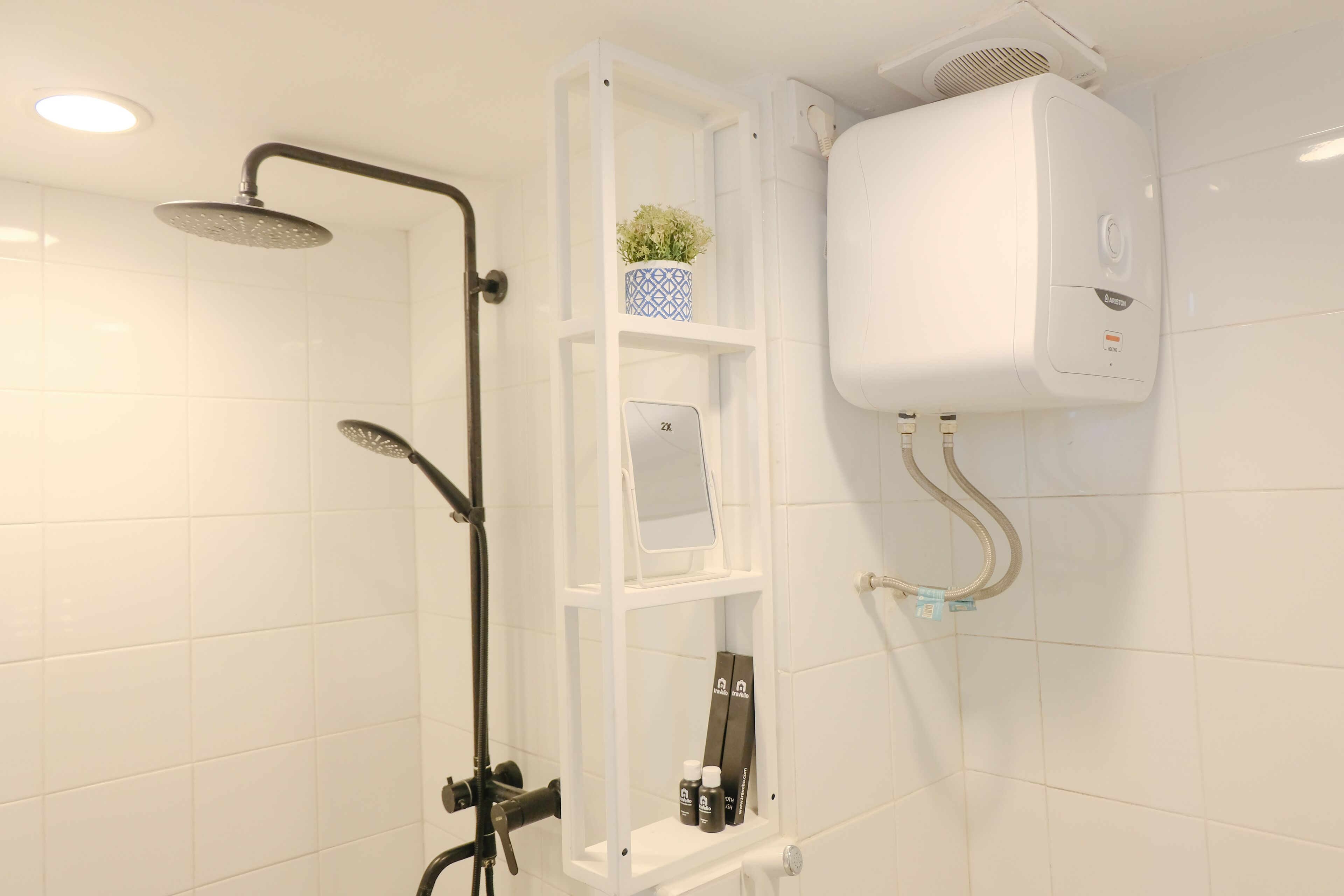 Kylpyhuone, jossa on suihku, valkoinen seinään kiinnitetty lämmitin ja hylly, jossa on hygieniatuotteita.