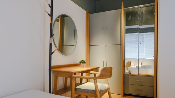 Un dormitorio con una cama, un escritorio de madera con una silla, una mesita con una planta y un armario con puertas correderas.