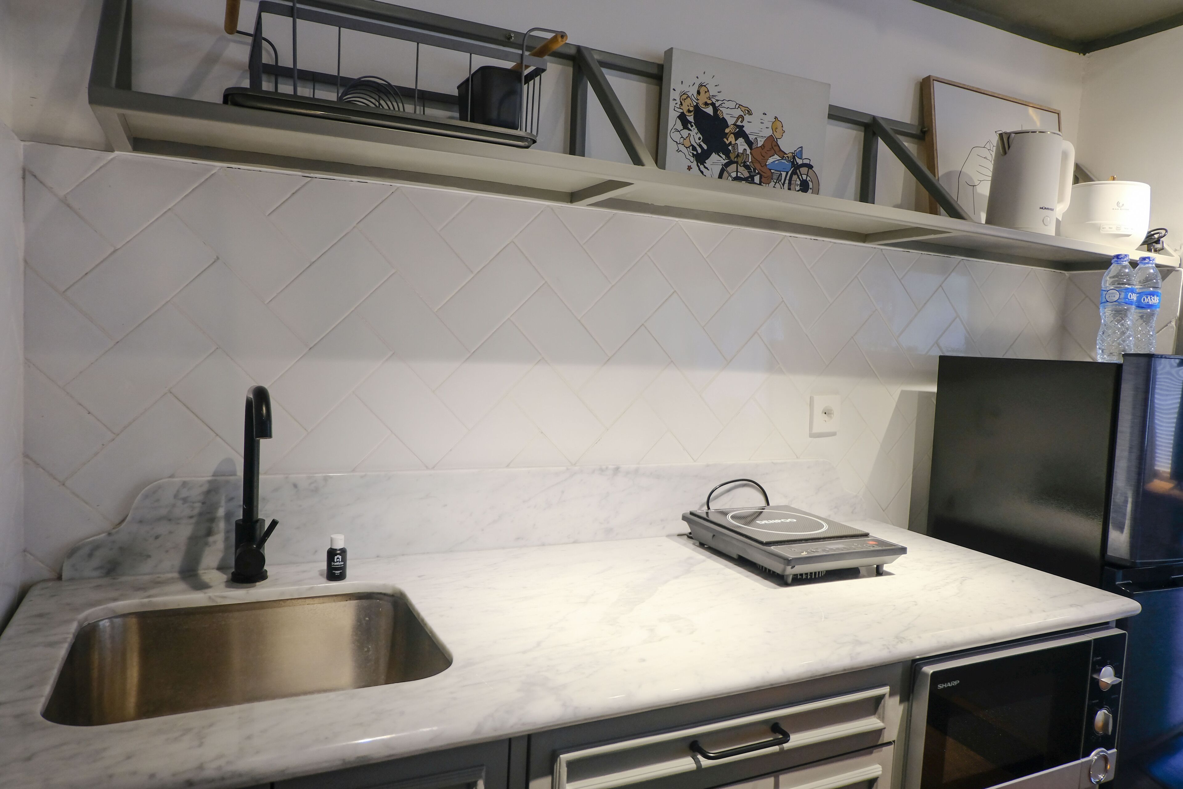 A kitchen with a stainless steel sink, a built-in oven, and a microwave. There is a water dispenser on the countertop.