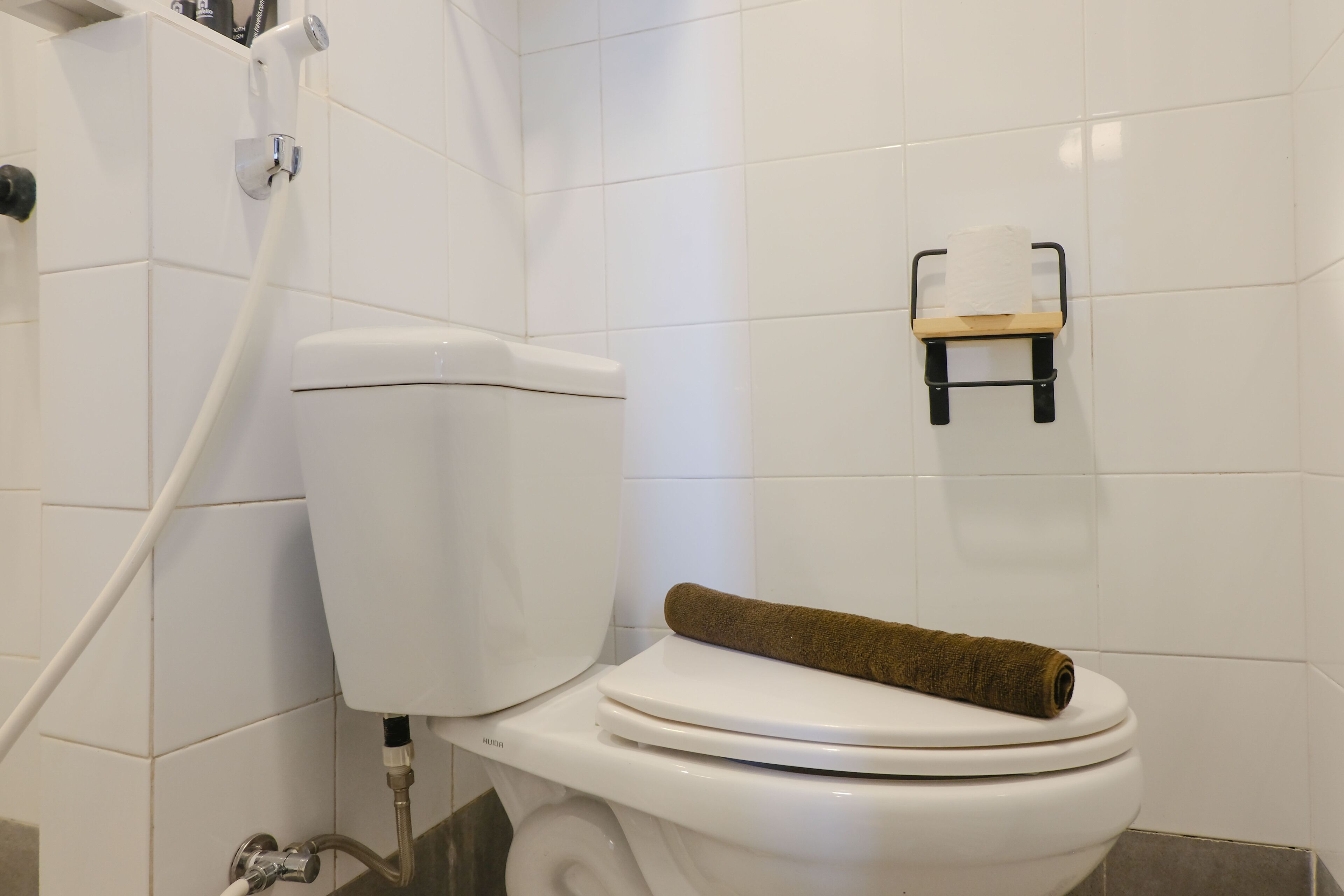 Un inodoro blanco con una toalla sobre el asiento, un dispensador de papel higiénico en la pared y un cabezal de ducha.