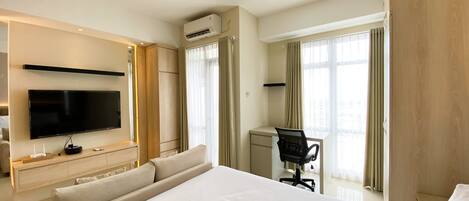 A hotel room with a large bed, a desk, a chair, a TV, and an air conditioning unit.
