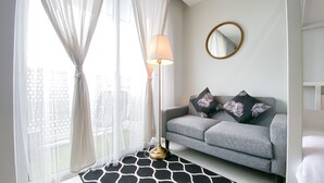 A modern living room with a grey sofa, two patterned pillows, a round mirror, and a floor lamp. - Modern Classic Studio At West Vista Apartment (Jakarta)
