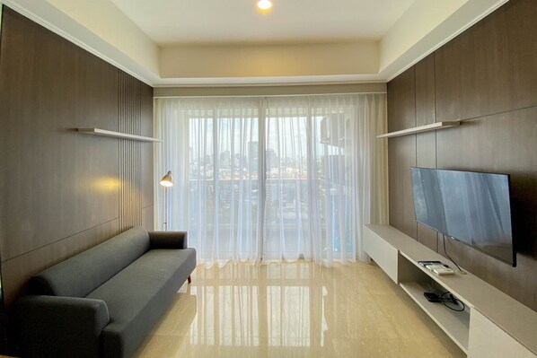 A modern living room with a sofa, a TV, and a city view through sheer curtains.