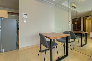 A modern kitchen with a refrigerator, a wall-mounted phone, and a dining area with a table and chairs.