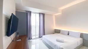 Une chambre d’hôtel moderne dotée d’un grand lit, d’un téléviseur à écran plat fixé au mur et d’une porte-fenêtre coulissante donnant sur un balcon.