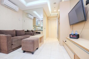 Una sala de estar moderna con sofá, reposapiés, televisor de pantalla plana y un kit de viaje sobre una mesa de madera.