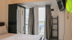 A hotel room with a bed, a wardrobe, a TV, and a balcony with curtains. - Comfy And Simply Studio Tokyo Riverside Pik 2 Apartment (Teluknaga)