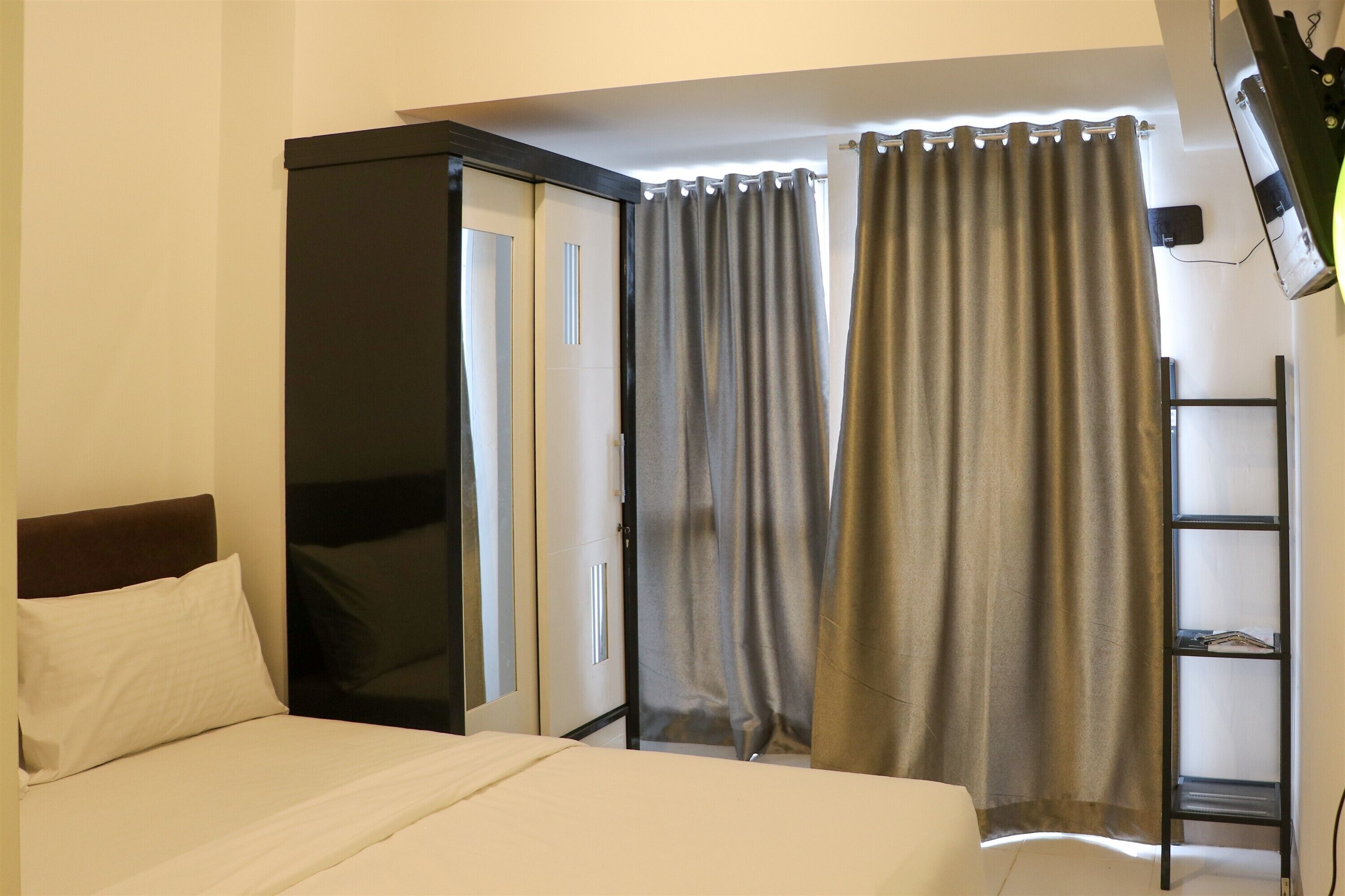 Hotellihuone, jossa on sänky, vaatekaappi, hylly ja verhot.