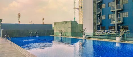 A swimming pool with a wooden deck and potted plants, surrounded by modern buildings and construction cranes.