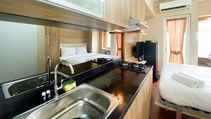 A compact hotel room with a kitchenette, a bed, a TV, and an air conditioning unit. - Cozy Stay Studio Room At Springlake Summarecon Bekasi Apartment (Bekasi)