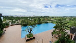 A rooftop pool with a wooden deck, surrounded by greenery and overlooking a cityscape. - Cozy Stay Studio At Sayana Bekasi Apartment (Tarumajaya)