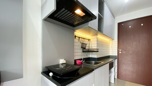A modern kitchen with a black countertop, stainless steel sink, and a wooden door. - Cozy Stay Studio At Sayana Bekasi Apartment (Tarumajaya)