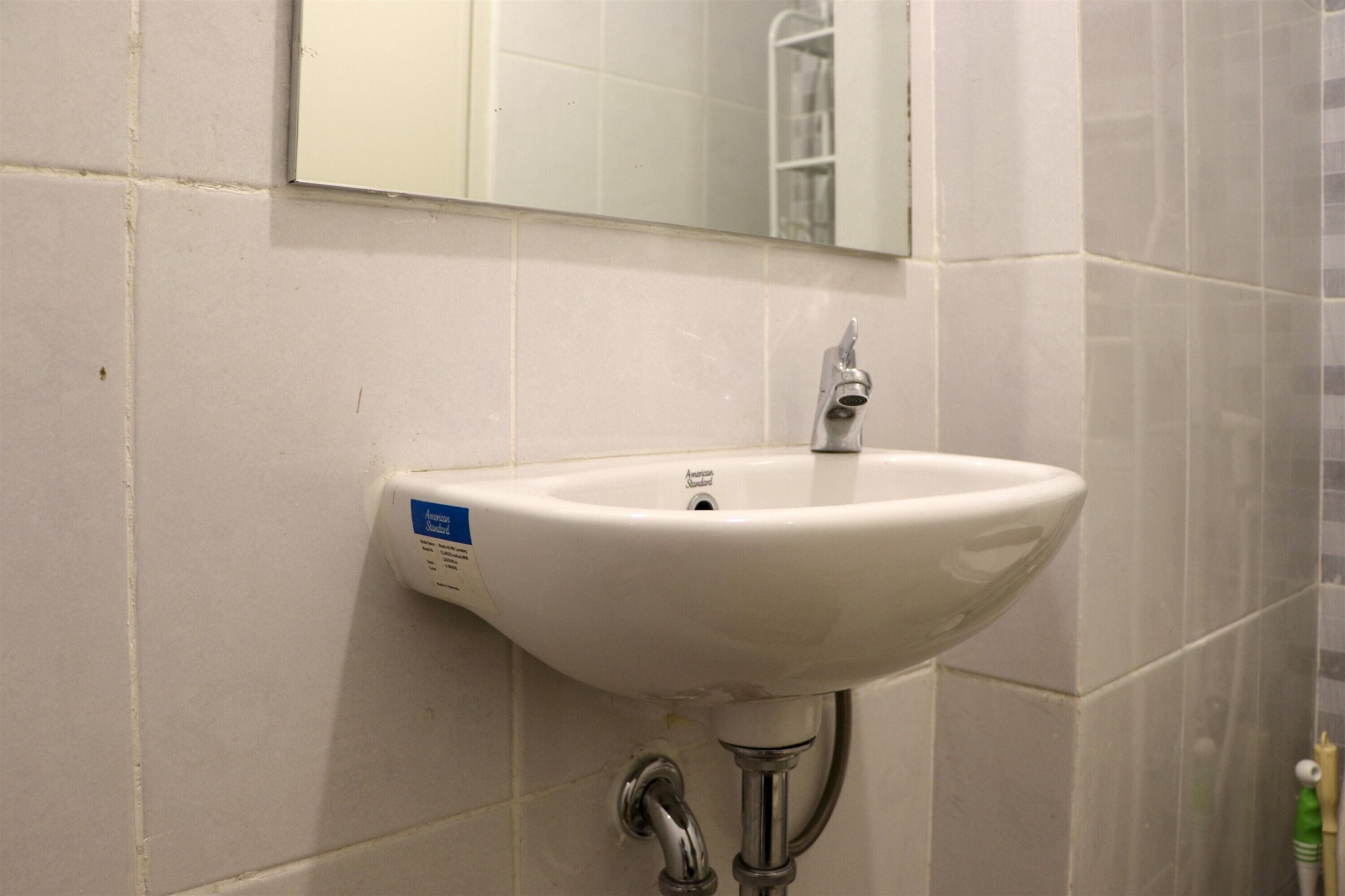 A white bathroom sink with a mirror above it, mounted on a tiled wall.