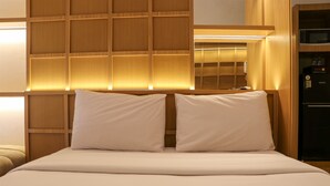 Une chambre d’hôtel avec une tête de lit en bois, un lit avec une literie blanche et un four à micro-ondes intégré.