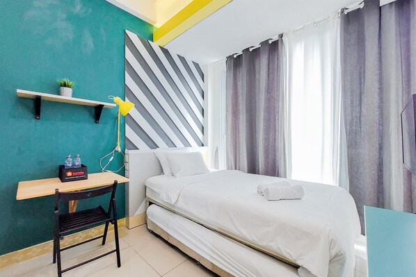 Een slaapkamer met een bed, een bureau, een stoel, een plankje met een plant en een lamp.