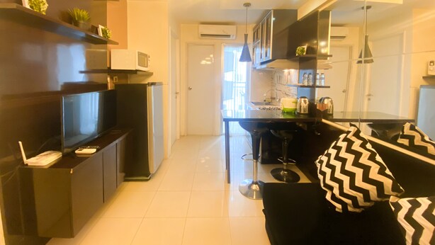 A modern kitchen with a central island, built-in appliances, and a dining area with a black and white patterned sofa. - Great Deal And Comfortable 2Br At Bassura City Apartment (Jakarta)