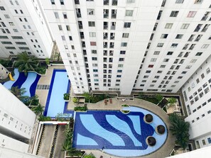 En høj bygning med flere balkoner og en central swimmingpool med et blåt bølgemønster.