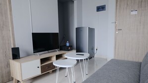 A modern room with a TV, two small tables, a sofa, and a tall appliance. - Homey 1Br Apartment At Newton Residence Bandung (Bandung)
