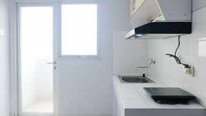 A kitchen with white tiles, a window, a sink, and a black countertop. - Homey 1Br Apartment At Newton Residence Bandung (Bandung)