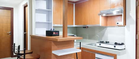 A compact kitchen with wooden cabinets, a built-in gas stove, and a small bar stool.