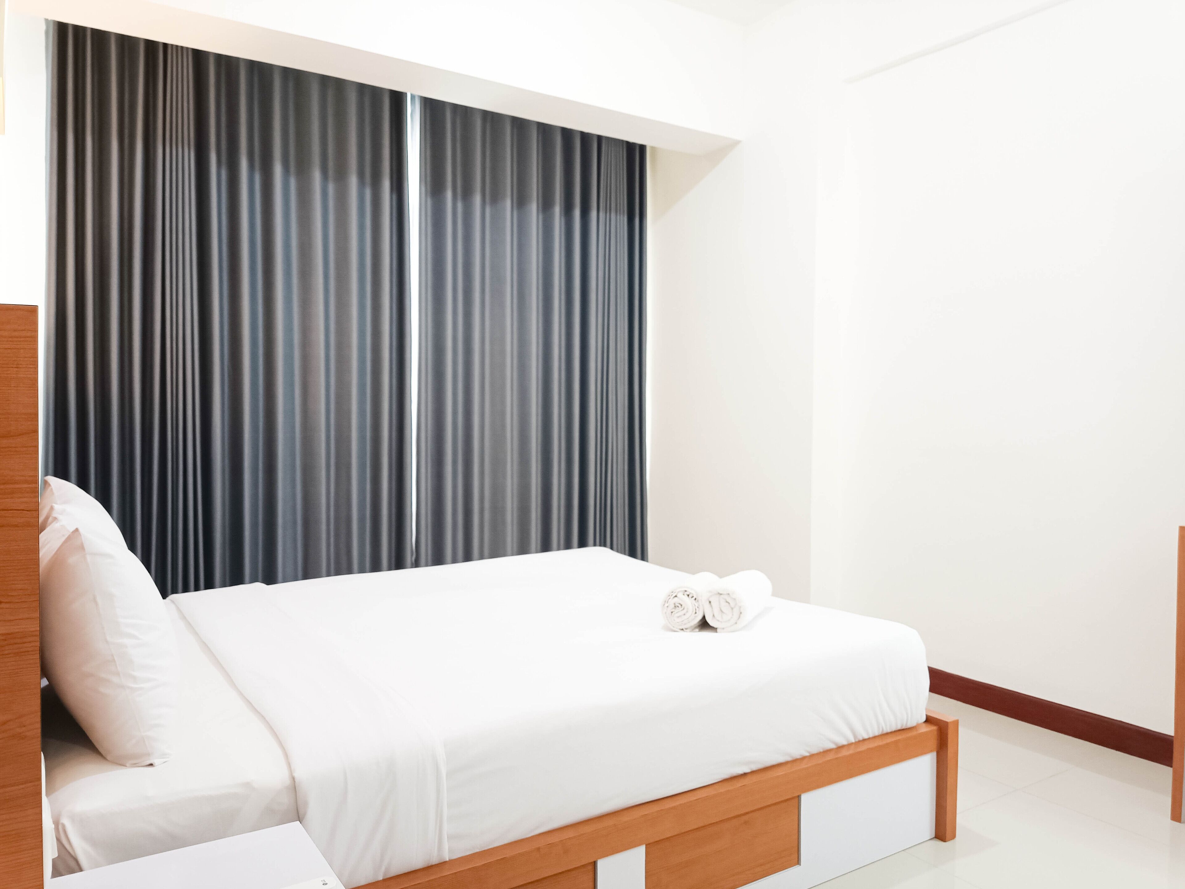 A modern bedroom with a wooden bed frame, white bedding, and dark curtains.