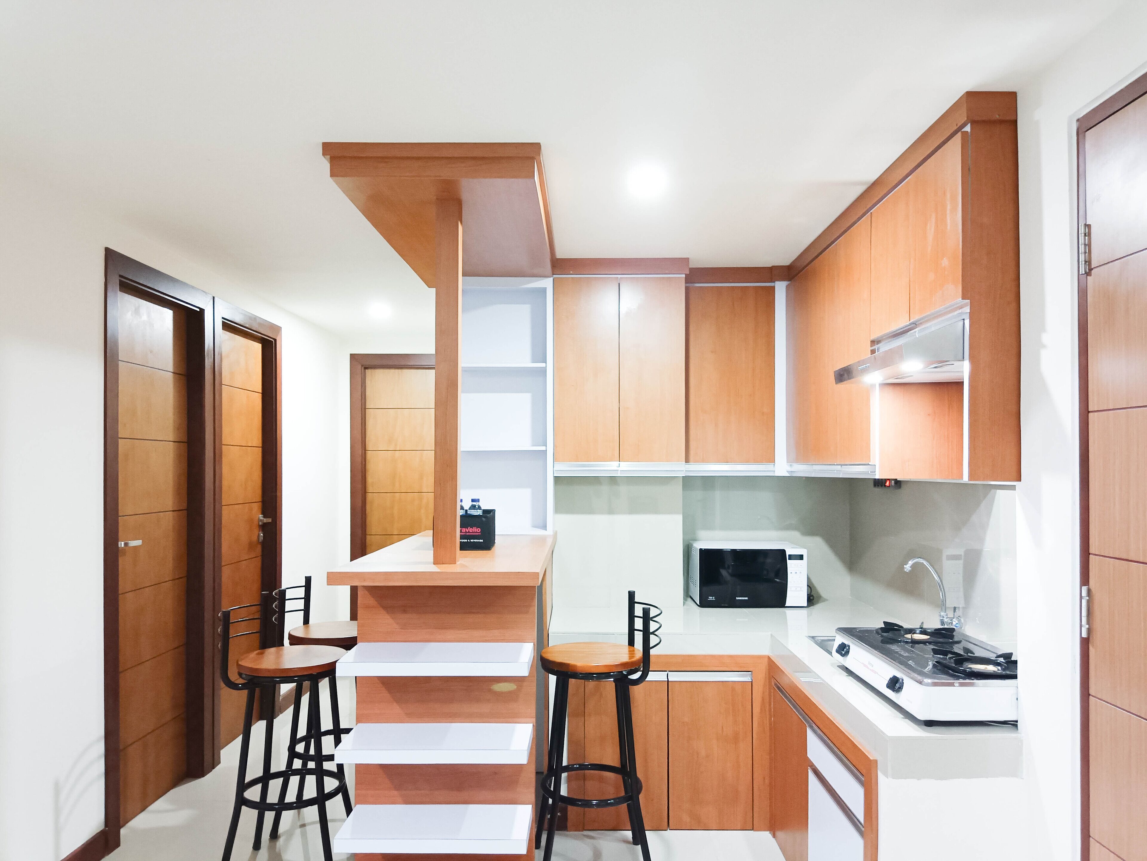 Une cuisine compacte avec des meubles en bois, un four à micro-ondes, une cuisinière et deux tabourets de bar.