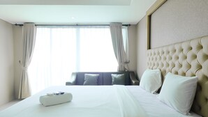 A hotel room with a large bed, a headboard, and a view of the outside through the window. - Good Choice Studio Apartment At Tamansari La Grande (Bandung)