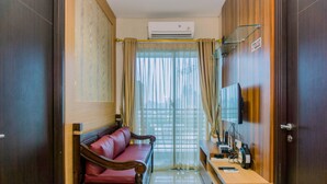 Een hotelkamer met een houten kledingkast, een rode bank, een klein bureau met een televisie en een airconditioning.