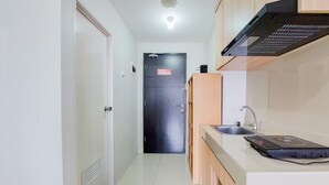 A narrow hallway leading to a door with a 'No Entry' sign, a small sink, and a microwave on the right. - Cozy Living Studio Room At Baileys Apartment (South Tangerang)