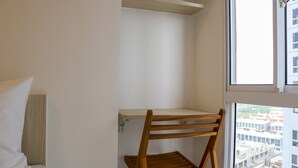 Eine Ecke eines Zimmers mit einem Holzstuhl, einem weißen Kissen und einem Fenster mit Blick auf Gebäude.