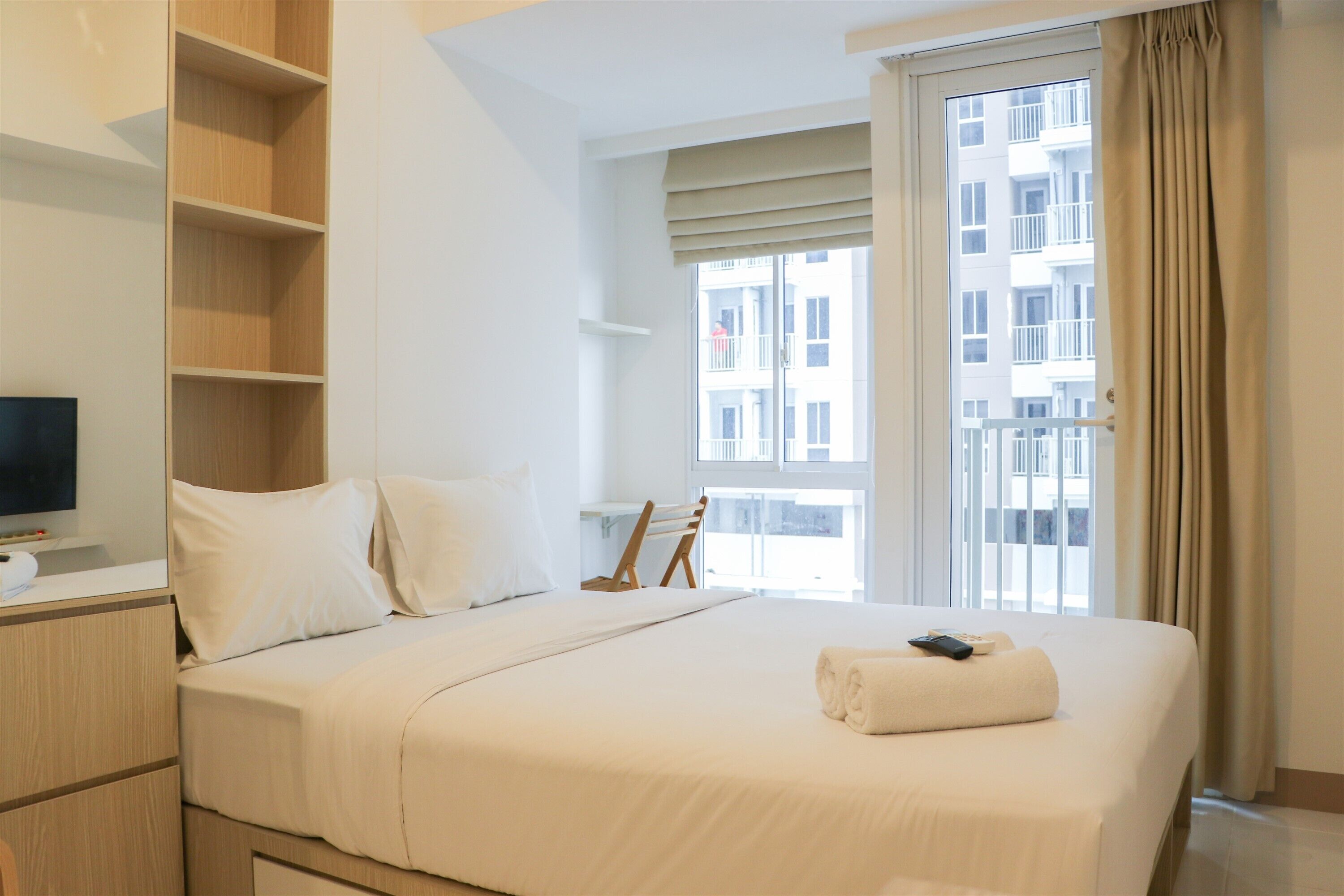 Une chambre d’hôtel avec un grand lit, un téléviseur posé sur un meuble, une armoire en bois et une fenêtre donnant sur un immeuble.