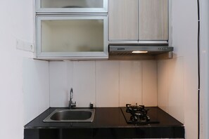 A compact kitchen with a gas stove, a stainless steel sink, and white cabinets with glass doors. - Cozy And Strategic 1Br At Gateway Pasteur Apartment (Cimahi)