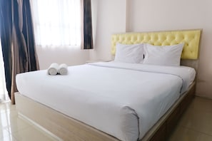 A neatly made bed with white linens and two rolled towels, a yellow tufted headboard, and a window with curtains. - Cozy And Strategic 1Br At Gateway Pasteur Apartment (Cimahi)
