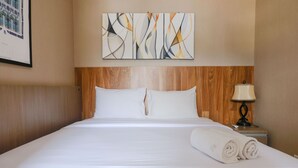 A hotel room with a large bed, wooden headboard, a wall-mounted abstract art piece, a bedside lamp, and neatly folded towels.