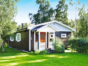 A single-story wooden house with a porch, surrounded by greenery.