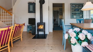 A spacious living area with a wooden staircase, a black wood stove, and a dining table with chairs. - 4 Person Holiday Home in Ringkobing (Ringkobing)