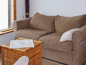 A brown sofa with a cushion, a small wooden stool with a cushion, and a window with a curtain. - 9 Person Holiday Home in Kalarne (Kälarne)