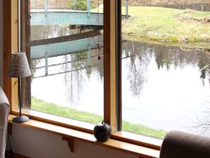 A room with a large window overlooking a pond and a wooden deck. - 9 Person Holiday Home in Kalarne (Kälarne)