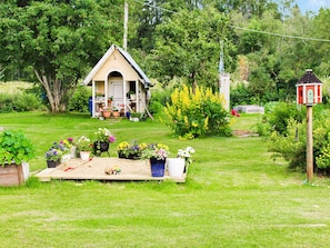 A small wooden structure with a pitched roof, surrounded by a variety of potted plants and flowers.