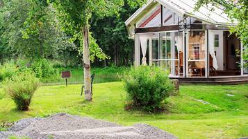A modern house with a glass facade, surrounded by lush greenery and a gravel path.
