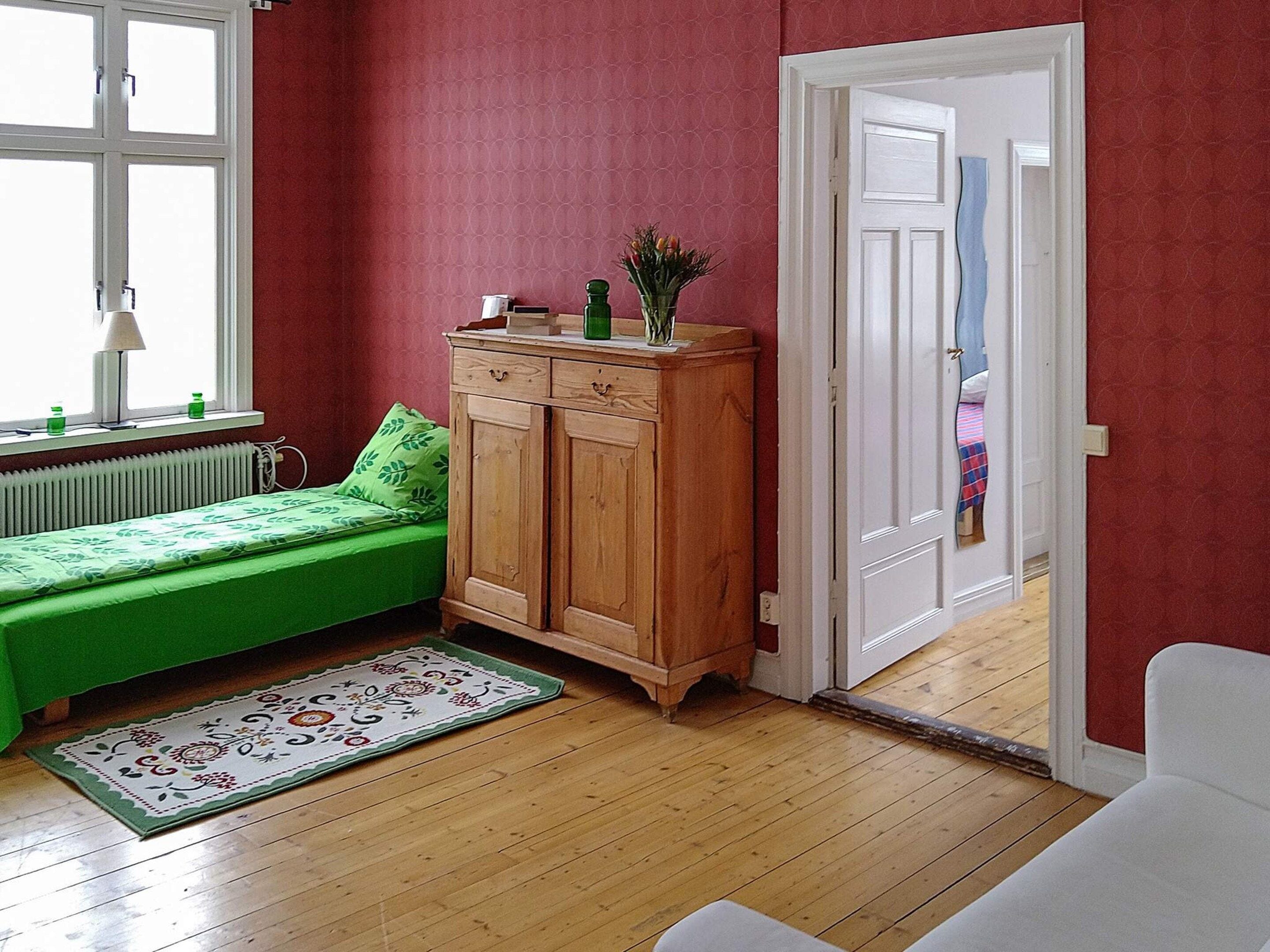 Une pièce avec un canapé vert, un meuble en bois, un radiateur et une porte qui donne sur une autre pièce.
